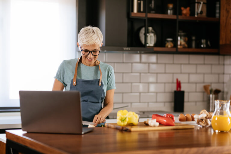 Senior woman preparing delicious lunch in the kitchen with the help of online recipe