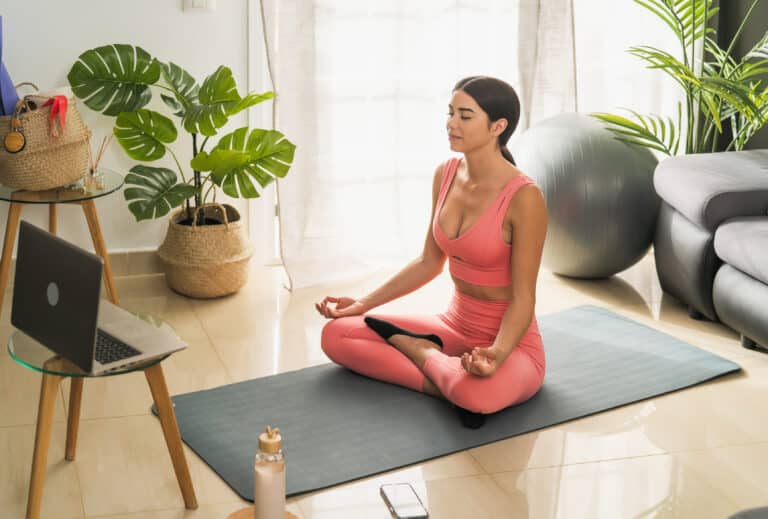 Latin young woman doing yoga virtual fitness class with laptop at home - E-learning and people wellness lifestyle concept